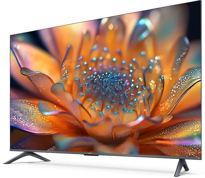 A sleek, bezel-less Xiaomi QLED TV FX Pro Series 2025 displayed in a modern living room, showcasing a vibrant 4K QLED screen with colorful visuals. The TV is placed on a minimalist stand, with the Alexa Voice Remote and a promotional banner highlighting key features like "4K QLED," "Dolby Audio," and "Fire TV OS" visible in the foreground.